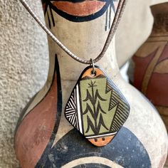 This vintage pottery pendant is a piece of art you can wear. It was made by Acoma potter Marilyn Ray, one of the Lewis sisters who learned pottery making from their mother, Katherine Lewis. Marilyn is the oldest sister and became known for her storytellers, but this is a rare piece of her jewelry. On the front it depicts the corn stalk, a sacred symbol to the Acoma and other Pueblo Indians. There are also geometric designs, and the color palette is lovely, in warm rust and sage green, black and white. The back is also painted, black and white with a striking symbol, and no matter which side shows, it is beautiful. I've paired this with a double chain necklace that is unusual, with cones seen in traditional Navajo jewelry and a liquid silver bead that is heavier than the type popular in the Artisan Hand Painted Green Necklace, Artisan Green Hand Painted Necklace, Artisan Green Hand Painted Necklaces, Vintage Hand Painted Brown Jewelry, Green Hand Painted Artisan Necklace, Hand Painted Brown Vintage Jewelry, Vintage Brown Hand Painted Jewelry, Brown Hand Painted Vintage Jewelry, Artistic Hand Painted Brown Jewelry