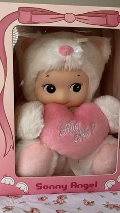 a pink and white teddy bear holding a heart in a pink box with the words hug me on it