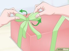 a person tying a green ribbon around a pink gift box