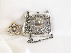 a silver purse sitting on top of a white cloth covered table next to a flower