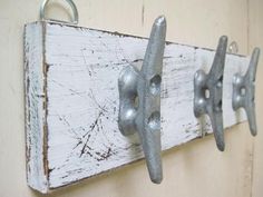 three metal hooks are hanging on a white wooden board with rusted paint and chipped paint