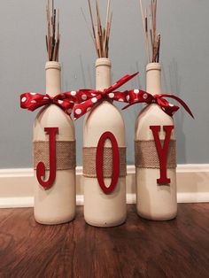 three wine bottles decorated with red ribbon and the word joy are sitting on a wooden floor