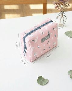 a pink cosmetic bag sitting on top of a white table next to a glass bottle