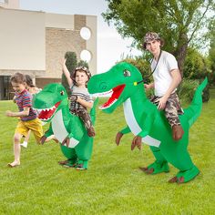 two children and an adult are playing with inflatable dinosaurs on the grass