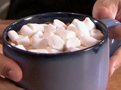 someone is holding a mug with marshmallows in it