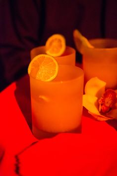 two glasses filled with orange juice and sliced lemons on a table next to an orange slice