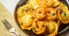 a black plate topped with pasta and shrimp next to a fork on top of a table