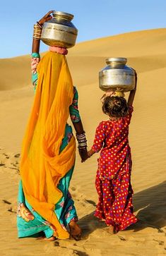 two women walking in the desert carrying pots on their heads