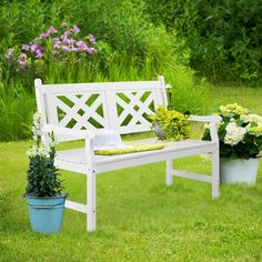 a white bench sitting in the grass next to potted plants and flowers on top of it