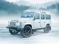 a white land rover is parked in the snow with trees in the backgroud