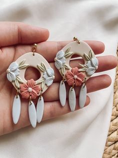 a hand holding three earrings with flowers and leaves hanging from the back of it's ear