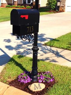 a black mailbox sitting on the side of a road next to a flower bed