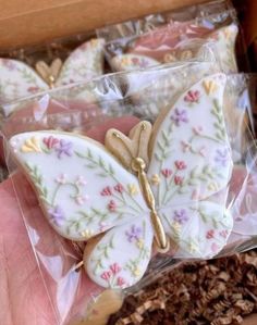 a hand holding some cookies in a box with flowers on it and a butterfly decoration