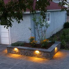 some lights that are on the side of a building in front of a tree and bushes