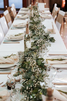 a long table is set with place settings and greenery for the centerpieces