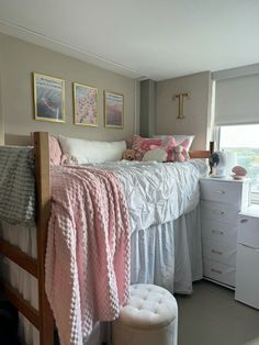 a white bed sitting next to a window covered in pink and white blankets on top of a wooden frame