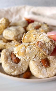 a hand is picking up some cookies from a plate with almonds on top and raisins in the middle