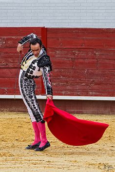 a man dressed in black and white with a red cape is performing a bullfight