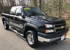 a black pickup truck with a green for sale sign on it's hood parked in front of some trees