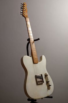 an old white guitar sitting on top of a black stand next to a gray wall