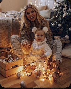 a woman sitting on the floor with a baby in her lap and christmas decorations around her