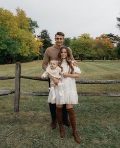 a man and woman holding a baby standing in front of a fence