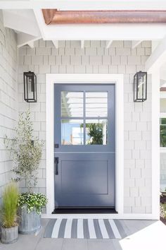 a blue front door with two planters on either side and a white brick wall behind it