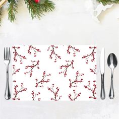 a place mat with red berries and silverware on it next to christmas greenery