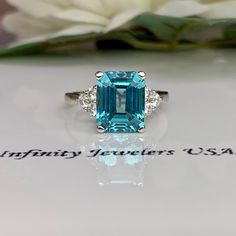 Paraiba Tourmaline Ring, Emerald Cut Engagement Ring 14K Gold, Three Stone Ring, Paraiba Ring For Ladies, Art Deco Paraiba Ring, #6311 This ring is an emerald cut lab created neon blue paraiba with round moissanite sides, 14k white gold # 6311 We feature the finest quality of lab grown stones in the world. The properties of lab-grown are physically, chemically and visually identical to natural, just grown in a lab setting. -Approximate total carat weight: 3.85ctw. diamond equivalent -Center Ston Gia Certified Sapphire Ring Gift, Gia Certified Oval Topaz Ring As Gift, Fine Jewelry Emerald Cut Topaz Ring Gia Certified, Gia Certified Emerald Cut Topaz Ring, Gia Certified Oval Topaz Ring For Gift, Gia Certified Radiant Cut Sapphire Ring Gift, Gia Certified Topaz Ring For Promise, Fine Jewelry, Luxury Tourmaline Round Cut Ring, Elegant Emerald-cut Tourmaline Ring