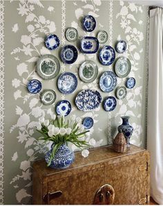 a wall with many plates on it and a vase in front of the plate display