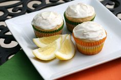 three cupcakes with frosting and lemon slices on a white plate next to an orange napkin