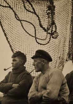 three men are sitting on a boat in the water and one is holding a pipe