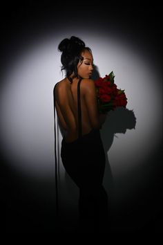 a woman in a black dress holding a bouquet of roses with her back to the camera