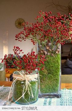 a vase filled with red flowers on top of a table next to another vase full of green plants