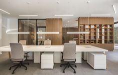 an empty conference room with two desks and chairs in front of a bookcase