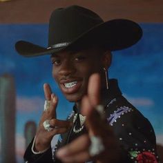 a man wearing a cowboy hat making the peace sign with his fingers in front of him