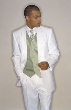 a man in a white suit and green tie is posing for a photo with his hands in his pockets