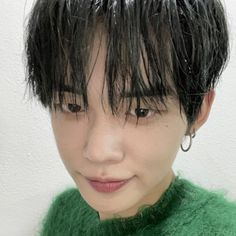 a close up of a person wearing a green sweater with black hair and piercings