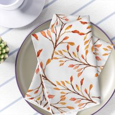 three napkins with leaves on them sitting on a plate next to a cup and saucer