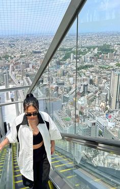 a woman walking up the side of a glass walkway in a high rise building with cityscape in the background