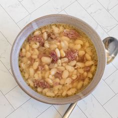 a bowl filled with soup sitting on top of a white tiled floor next to a spoon