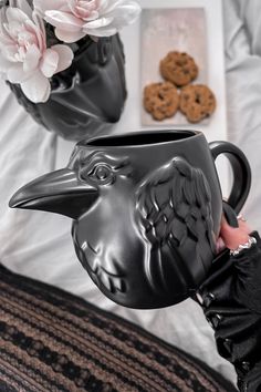 a person is holding a black mug with a bird head on it and cookies in the background