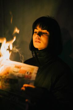 a woman reading a newspaper in the dark with flames coming out of her face and behind her