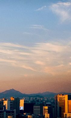 an airplane flying in the sky over a city with tall buildings and mountains behind it