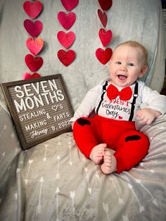 a baby sitting on top of a bed with hearts hanging from the wall behind him