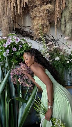 a woman in a green dress kneeling next to some plants and flowers on the ground