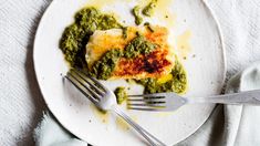 a white plate topped with meat covered in sauce and pesto next to a fork