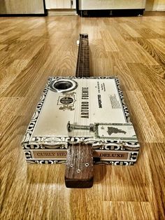 an old guitar laying on the floor in a kitchen with hard wood floors and white cabinets