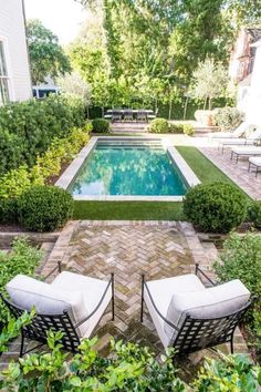 two chairs sitting in front of a swimming pool surrounded by greenery and bushes with trees