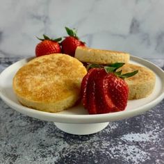 two biscuits and three strawberries sit on a white plate with marble countertop in the background